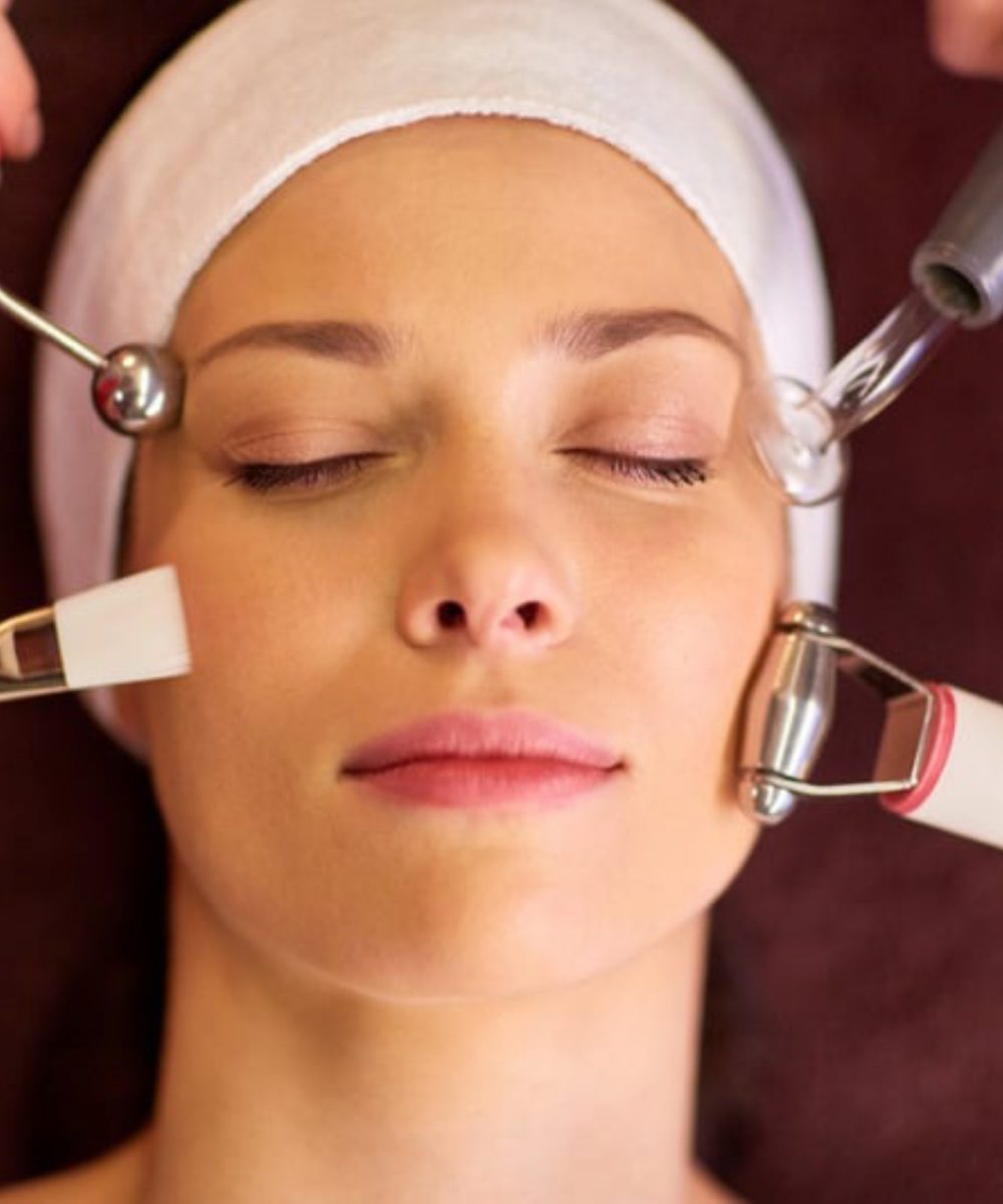 Woman receiving multi-device facial treatment with microcurrent and glass electrode for radiant skin at clinic