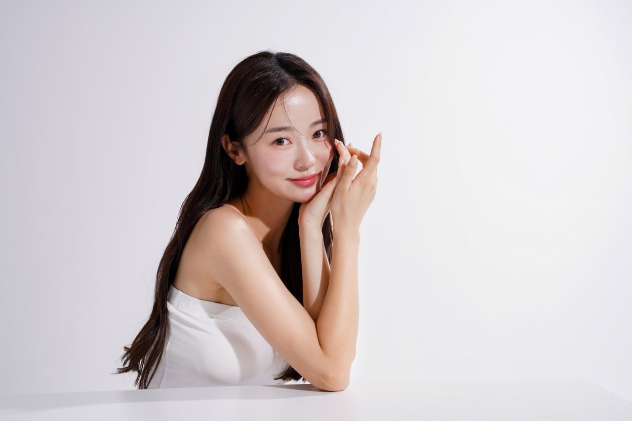 Young woman with glowing, camera-ready skin gently touching her cheek to showcase luminous, refined complexion