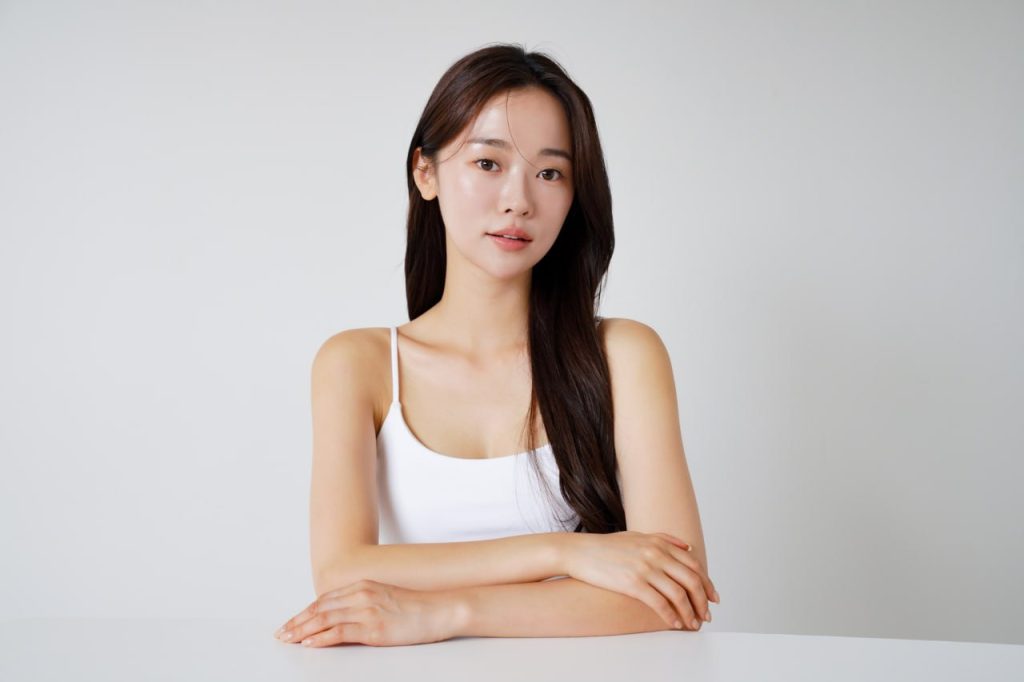 Woman with glowing, even-toned skin in white camisole seated at table representing Daily Glow skincare treatment