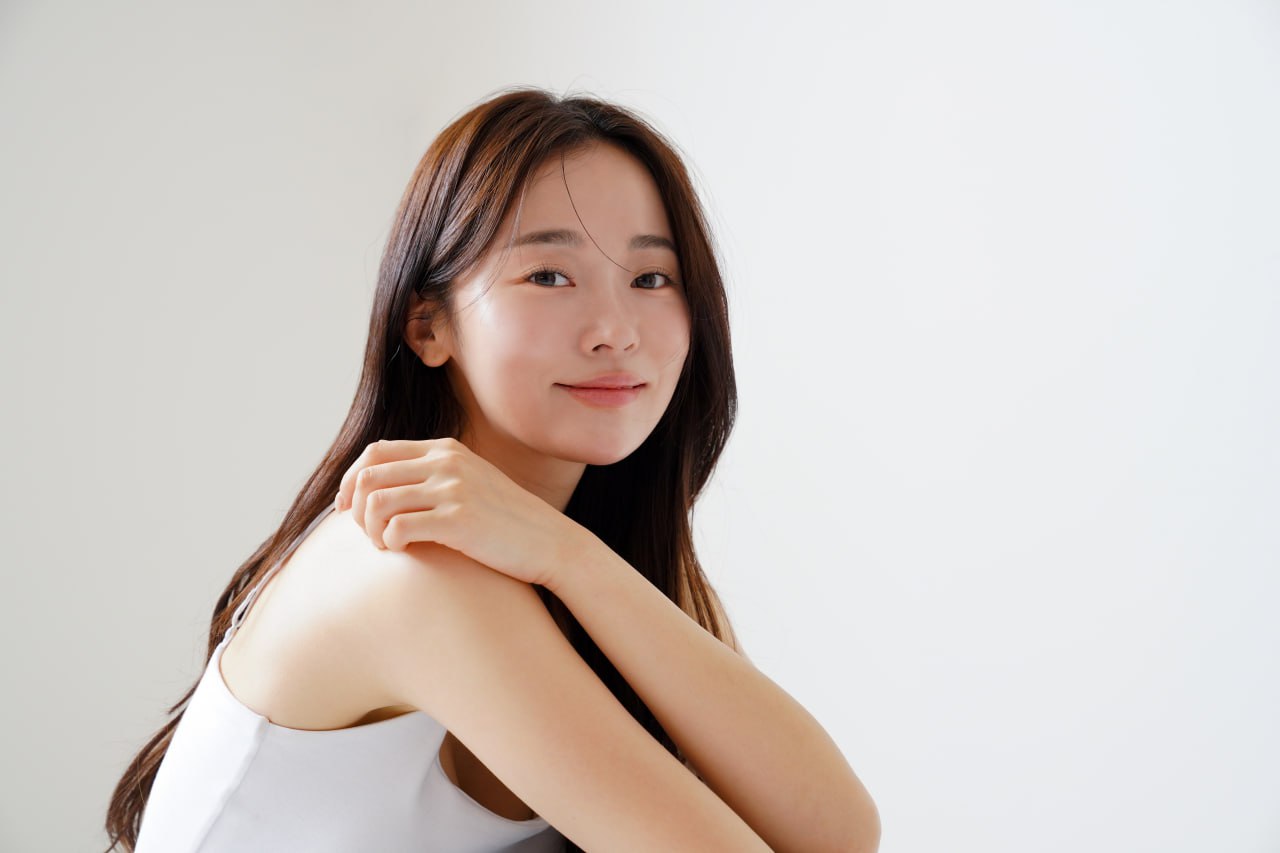 Young woman with radiant, clear skin smiling over shoulder showcasing hydrated luminous complexion for Daily Glow