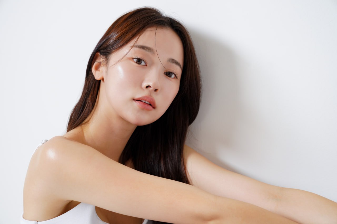 Close-up of a young woman with dewy, luminous skin leaning against a white wall, showcasing a daily glow skincare result
