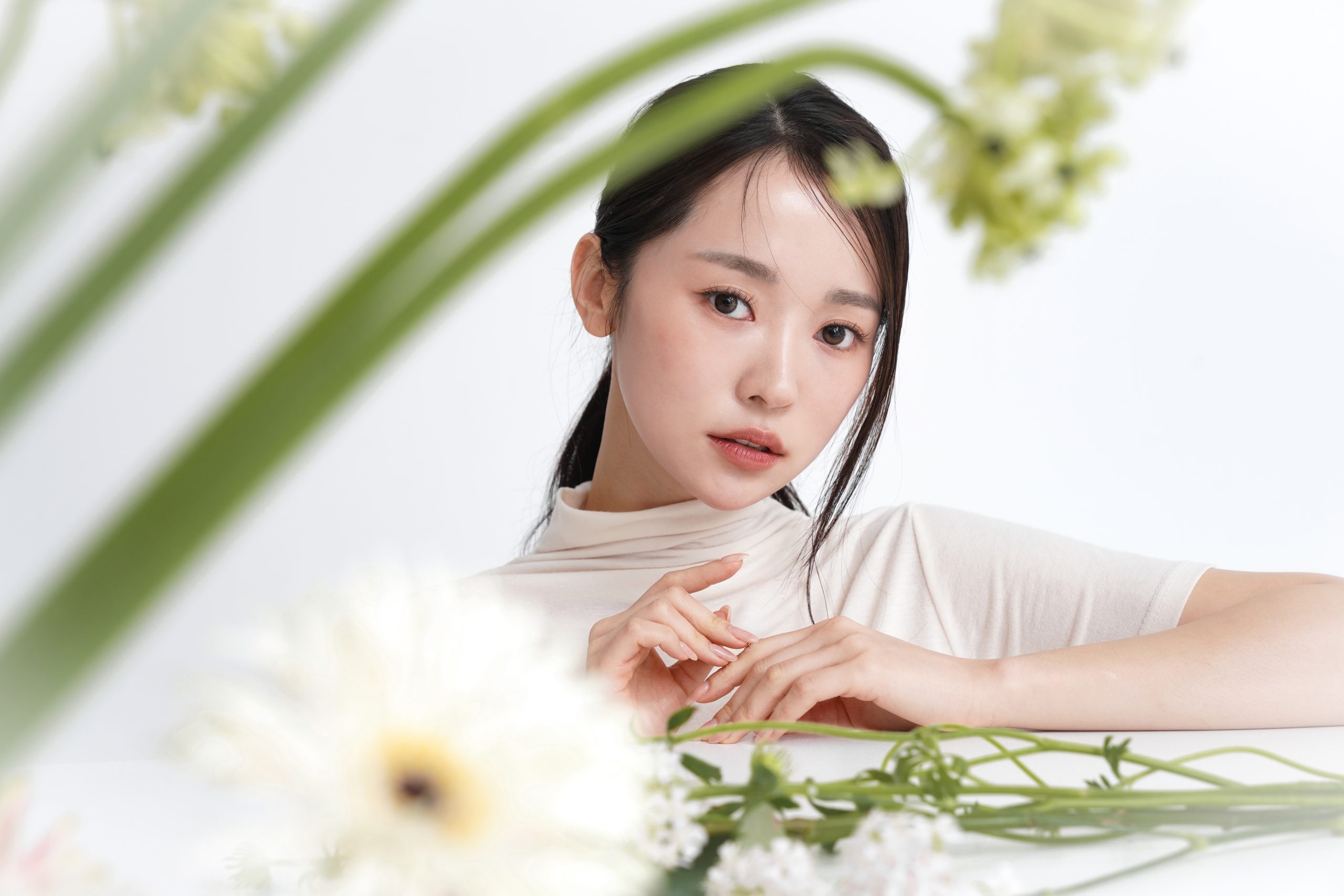 Close-up of a young woman with glowing skin posing among soft white flowers, highlighting smooth complexion for Peel & Fill