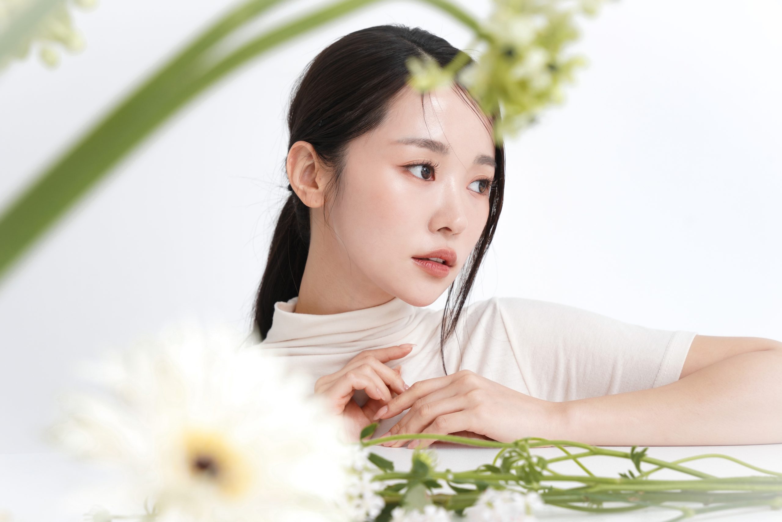 Young woman with dewy, clear skin posing among white flowers, highlighting smooth texture for Peel & Fill treatment page