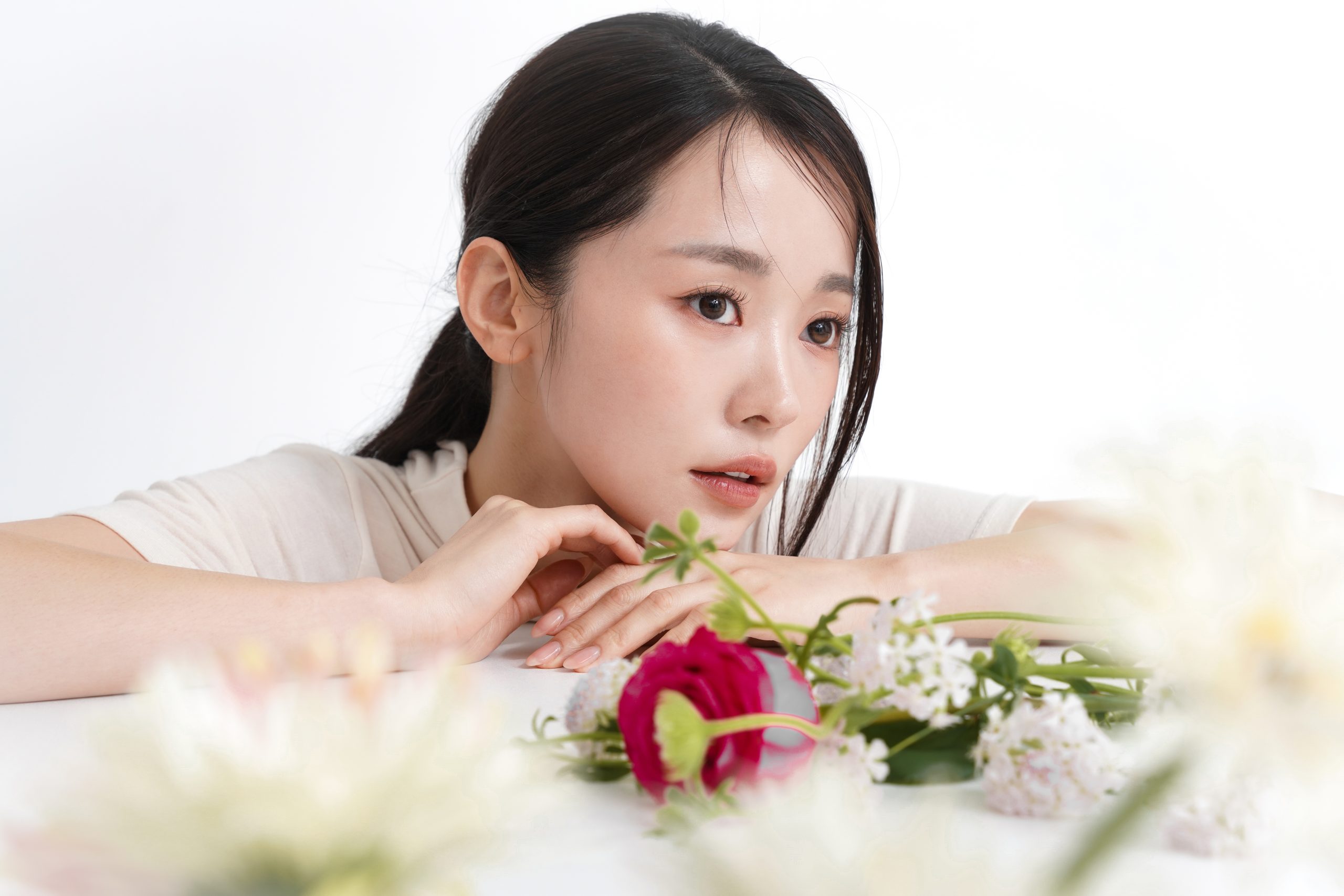 Close-up of a young woman with flawless skin resting on hands beside flowers for Peel & Fill skin reset treatment page