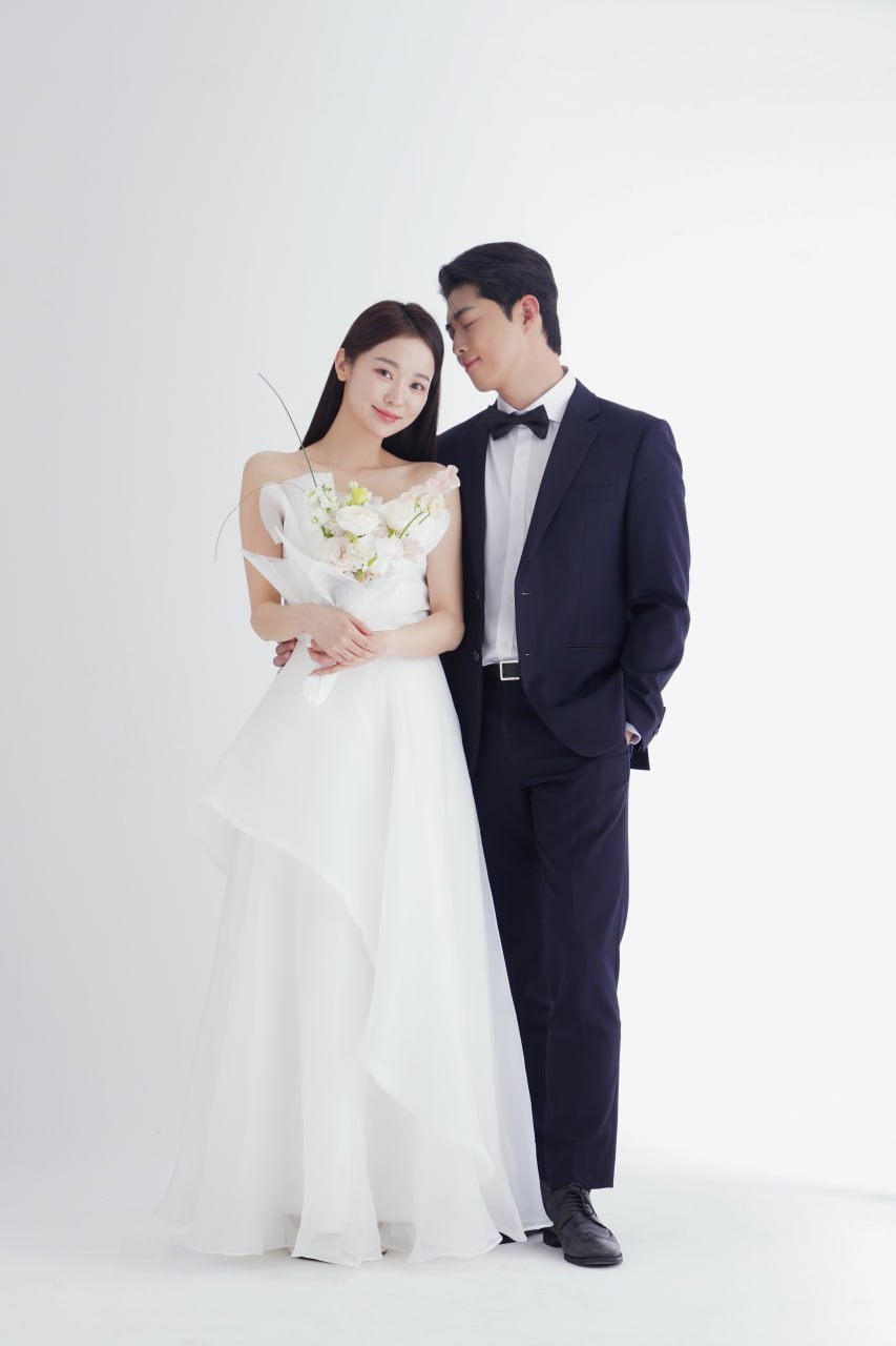 Bride in off-shoulder white gown holding bouquet with groom in navy suit beside her for a photo-ready special occasion