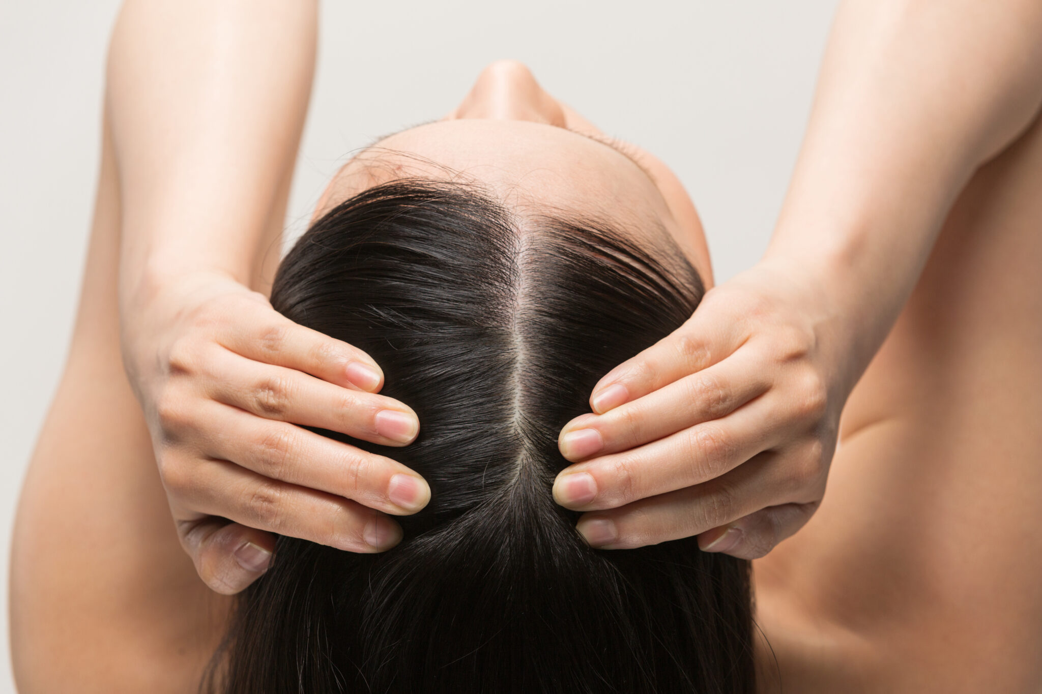 Woman lying back with hands massaging a clean central scalp part to illustrate hair regeneration and scalp care program