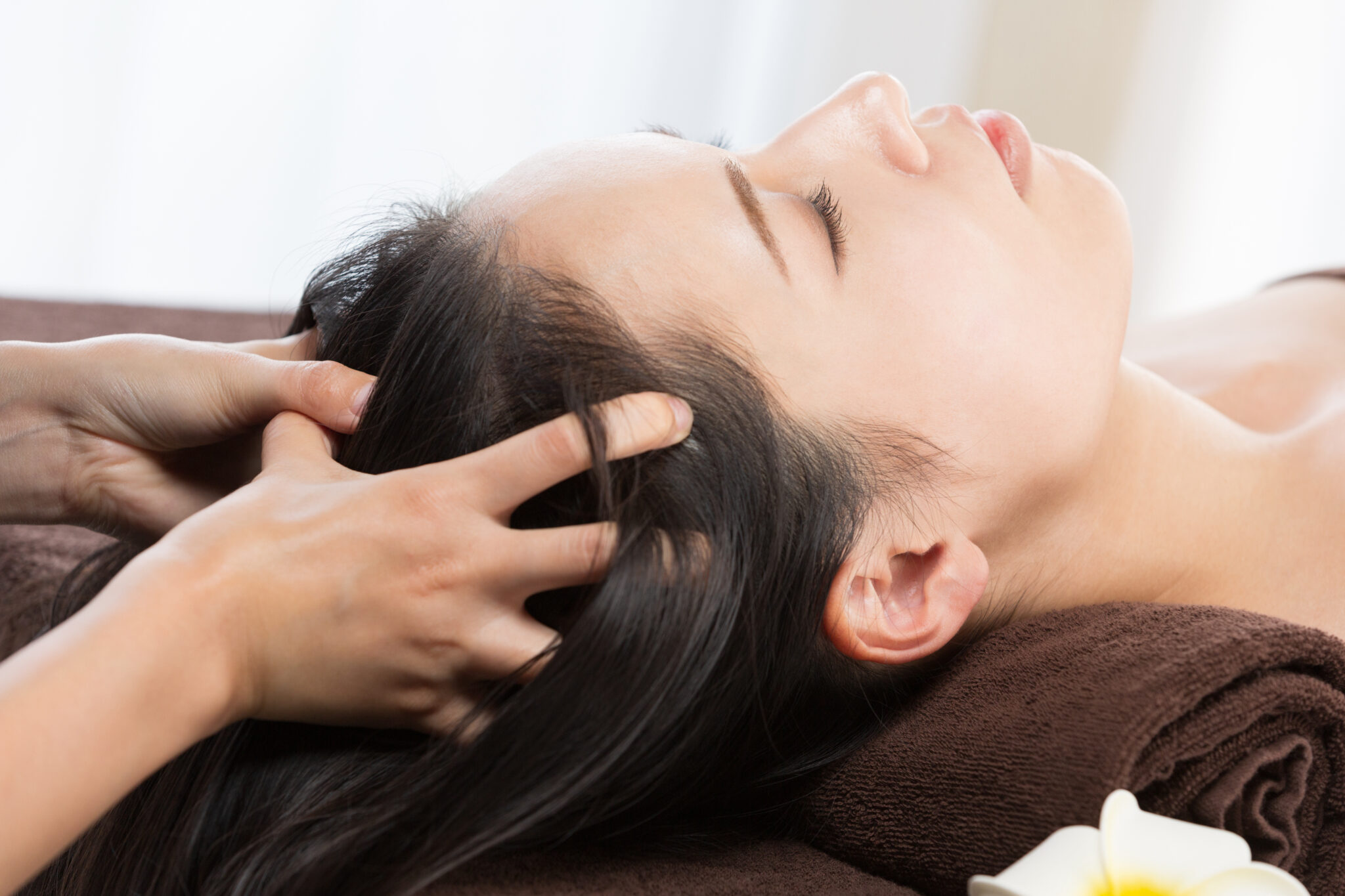 Woman lying with eyes closed receiving a gentle scalp massage for hair regeneration and scalp health clinic treatment