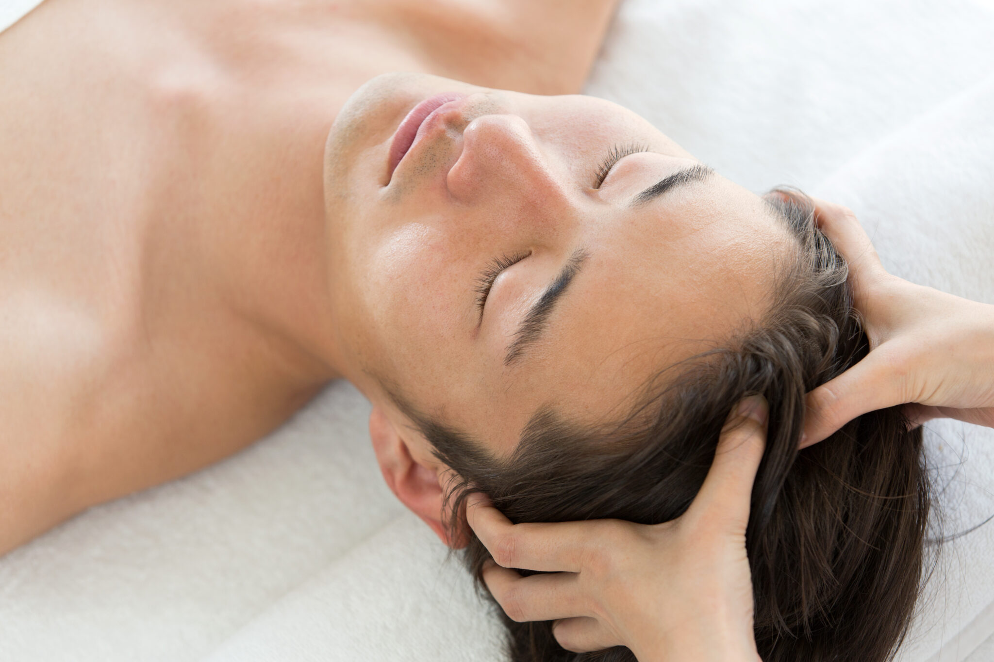 Young man receiving gentle scalp massage therapy for hair regeneration and scalp health at a dermatology clinic
