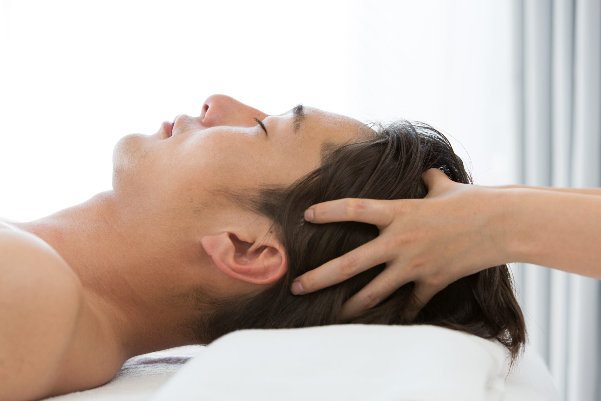 Close-up of a young Asian man receiving a gentle scalp massage for hair regeneration and scalp health clinic treatment