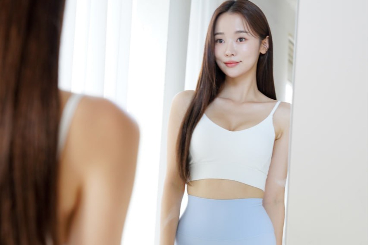 Young woman in activewear checking her clear skin in a mirror, representing sports skincare for active lifestyles