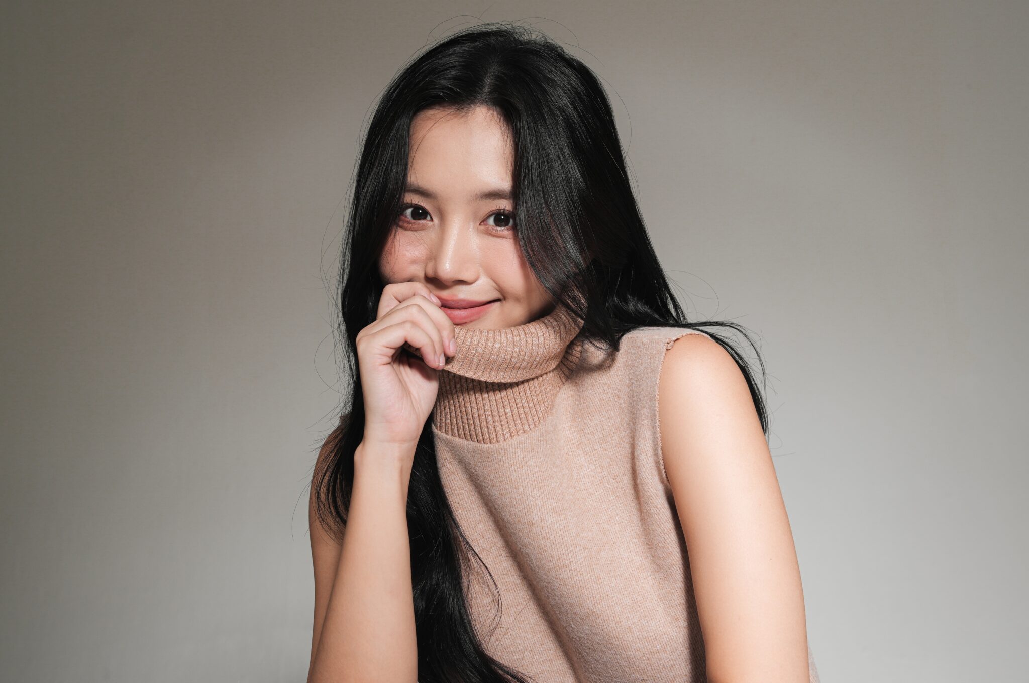 Young Asian woman in a beige turtleneck sweater smiling with clear glowing skin, portrait for VVIP skincare package