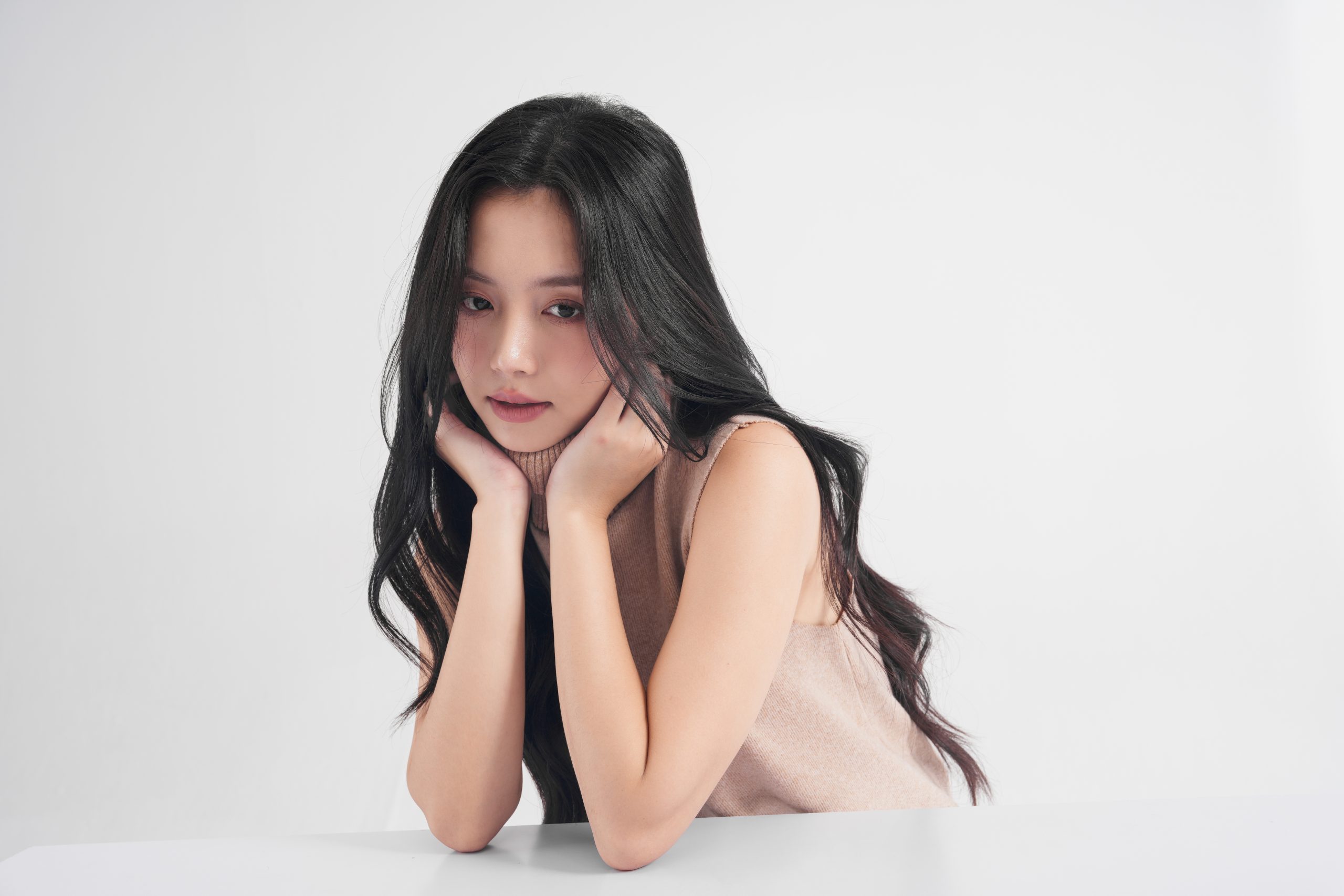 Young Asian woman in a beige sweater with clear radiant skin posing thoughtfully for VVIP skincare promotion