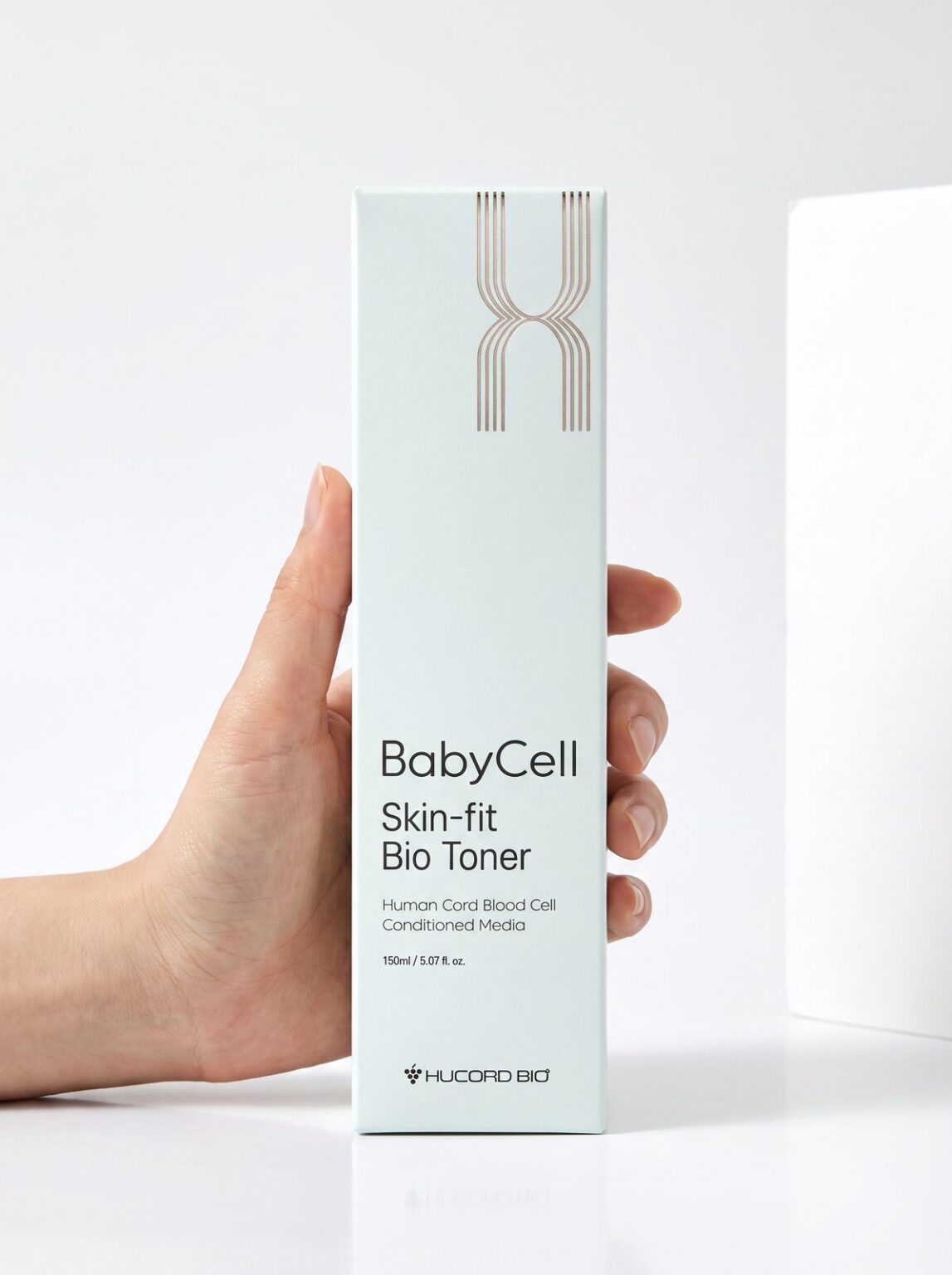 A hand holds a mint green box of BabyCell Skin-fit Bio Toner 150 ml by Hucord Bio against a white background.